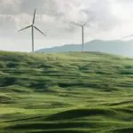 Windräder auf einer grünen Wiese vor Bergen